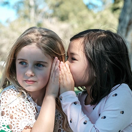 Photo of two girls with one whispering a secret to the other