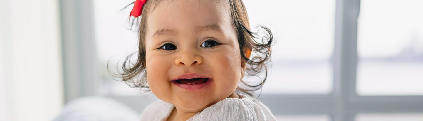 Baby girl with red ribbon smiling at camera.