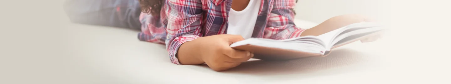 Cropped view of a child reading a book while laying down