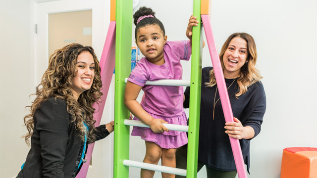 Two therapists supporting child climbing a ladder